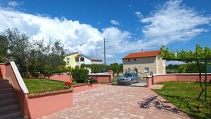 A residential area with a paved driveway leading to a house with a red roof, a staircase, and a garden with flowers. - Apartment 1875 (Marcana)
