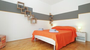 A bedroom with a bed, a nightstand, a wooden staircase, and a herringbone-patterned floor. - Apartment 1875 (Marcana)