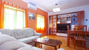 A living room with a sofa, coffee table, TV, and wooden cabinets. - Apartment 1875 (Marcana)
