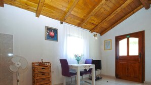 A room with a wooden ceiling, a white fan, a table with chairs, a wicker basket, a television, and a wooden door with a sign.