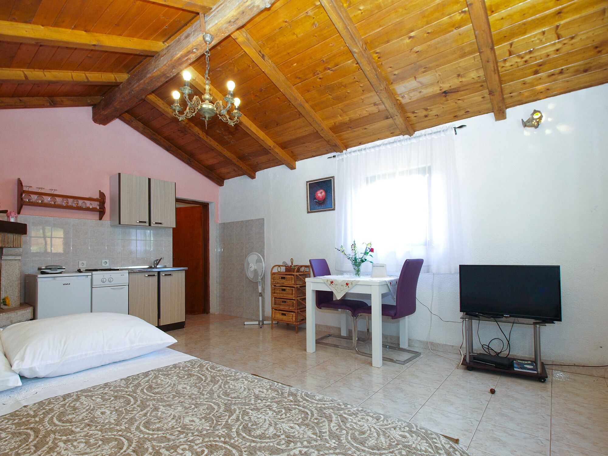 A cozy room with a wooden ceiling, a dining area with a table and chairs, a TV on a stand, and a kitchen with cabinets and a sink.