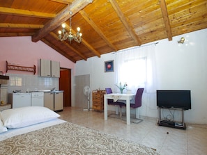 A cozy room with a wooden ceiling, a dining area with a table and chairs, a TV on a stand, and a kitchen with cabinets and a sink.