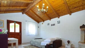 A bedroom with a wooden ceiling, a bed with a patterned bedspread, a small bedside table, a nightstand, and a decorative fireplace.