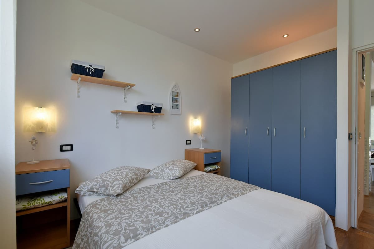 A bedroom with a bed, two nightstands, a wardrobe, and wall-mounted shelves.