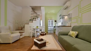 Un soggiorno moderno con un divano verde, sedie bianche, un tavolino in legno e una scala decorata con piante.