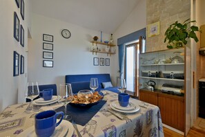 Un rincón comedor acogedor con una mesa preparada para cuatro, un sofá azul y una zona de cocina con estantes.