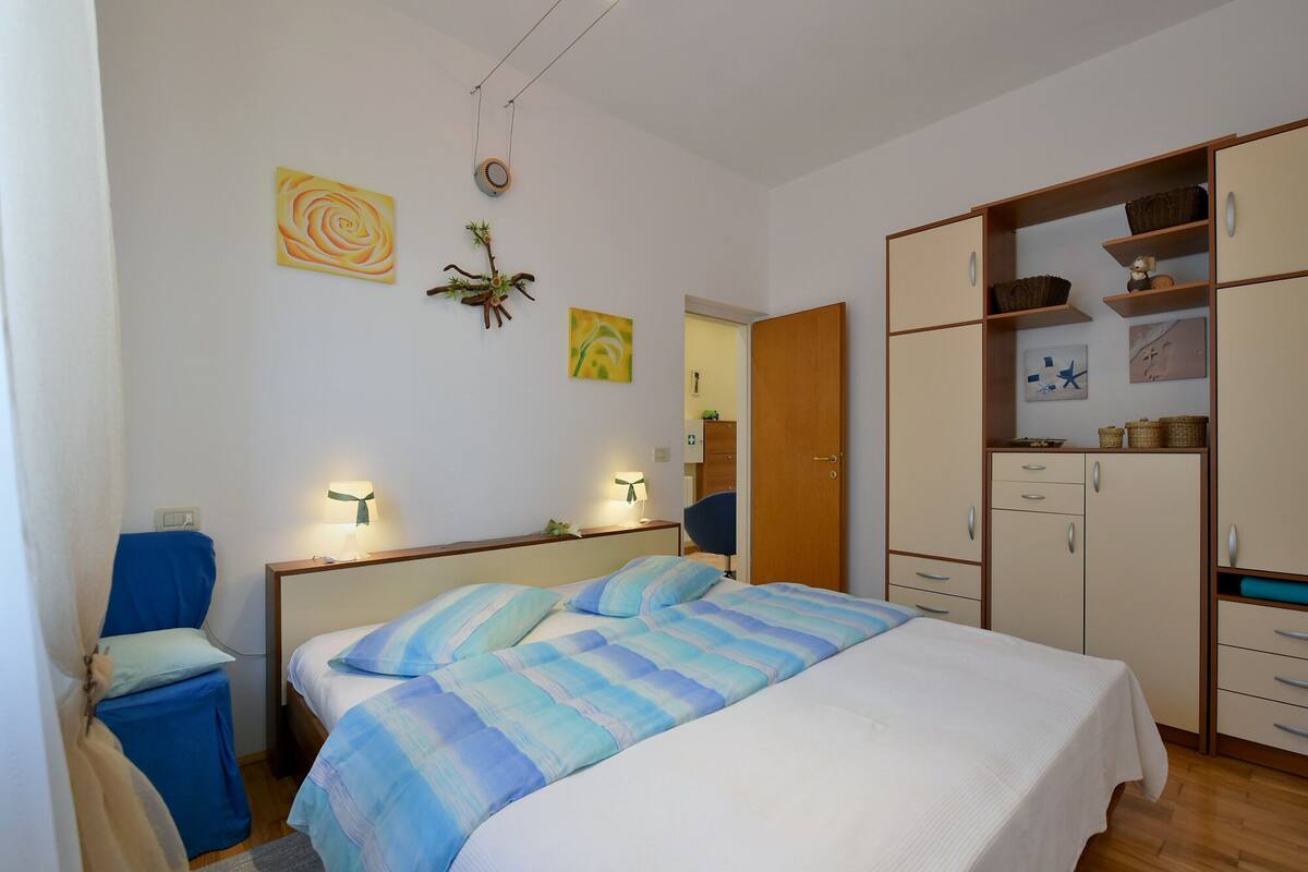 A bedroom with a bed, bedside lamps, a wardrobe, and a desk with a chair.