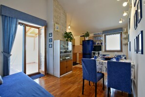 Un espacio habitable compacto con comedor, kitchenette y un dormitorio con puerta corrediza a un balcón.