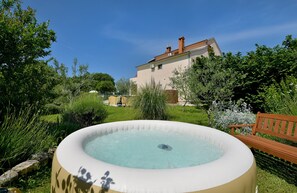 A hot tub in a lush garden with a house in the background. - Apartment 1877 (Vodnjan)