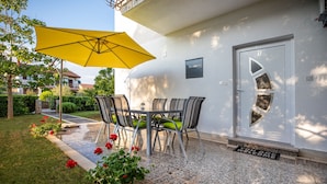 Un patio con una mesa y sillas, una sombrilla amarilla y un felpudo.