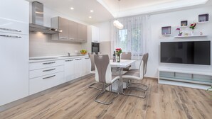 Una cocina moderna con armarios blancos, una mesa de comedor con sillas, un televisor integrado y una ventana con cortinas.