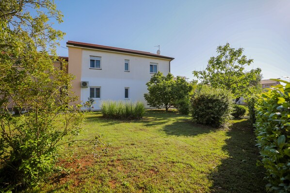 A two-story building with a flat roof, surrounded by a well-maintained lawn and various shrubs.