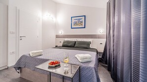 Ein modernes Hotelzimmer mit einem ordentlich bezogenen Bett, einem kleinen Tisch mit Obstschale und einem Weinglas, sowie einem Gemälde an der Wand.