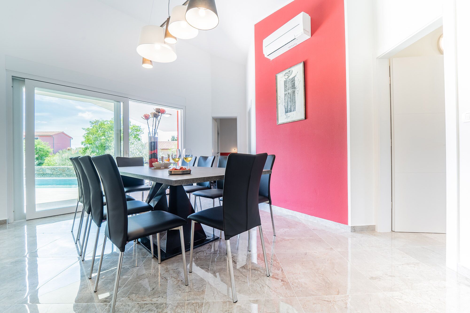 Un espace repas avec une grande table, des chaises noires et un mur d’accent rouge.