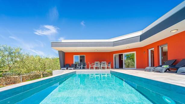 Ein modernes Haus mit Swimmingpool, Sitzgelegenheiten im Freien und blauem Himmel.