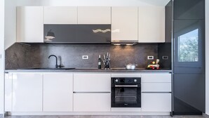 Eine moderne Küche mit eingebautem Backofen, einer Spüle aus Edelstahl und einem Fenster, das für natürliches Licht sorgt.