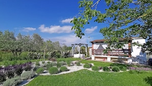 A well-maintained garden with a gazebo, a white building with a red roof, and a clear blue sky. - House 1884 (Fazana)