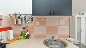 A kitchen with a stainless steel sink, hanging utensils, and a tiled backsplash. - House 1884 (Fazana)