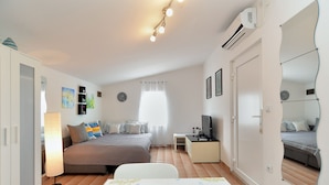 A well-lit bedroom with a bed, bedside table, TV, and a dining area with a table set for two. - House 1884 (Fazana)