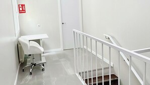 A clean, modern hallway with a white floor, a white railing, and a door at the end. - Hostel 18 (Madrid)