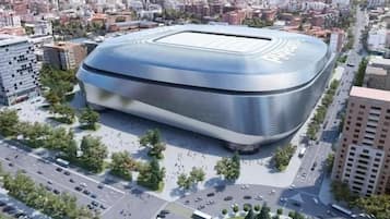 A modern stadium with a curved roof, surrounded by urban buildings and roads.