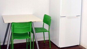A white refrigerator, a green chair, and a small table in a corner of a room. - Hostel 18 (Madrid)