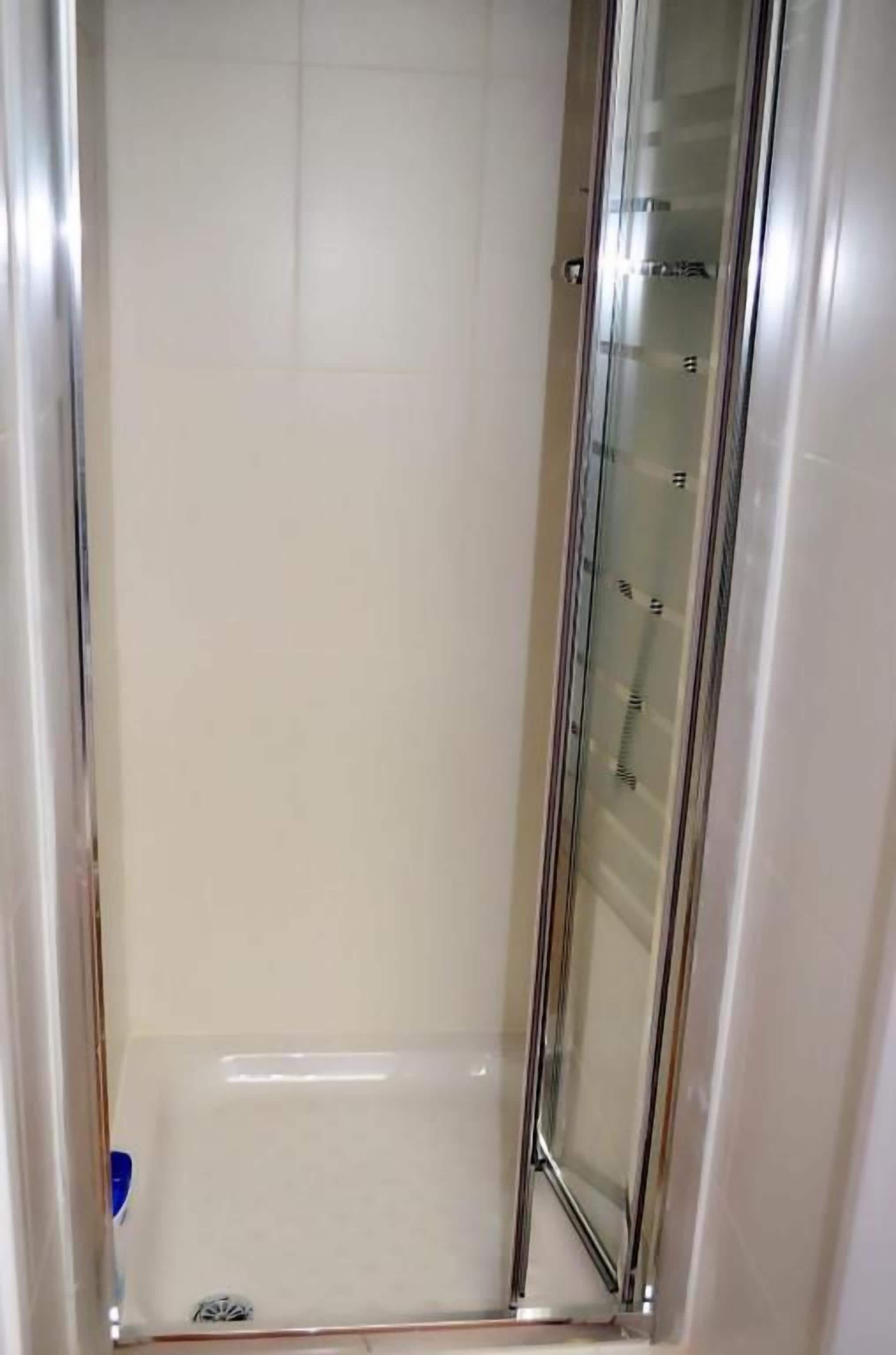 A glass-enclosed shower stall with a tiled floor and a metal frame.