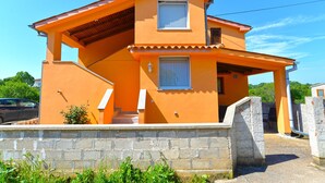 Una casa de dos pisos con techo inclinado, un porche cubierto y un muro de piedra al frente.