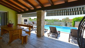 Un espacio al aire libre cubierto con una piscina, mobiliario de madera y pilares de piedra.