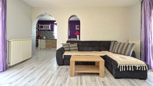 Una sala de estar con un sof á oscuro, una mesa de centro de madera y cortinas moradas.