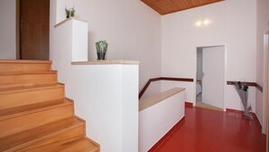 A staircase with wooden steps leading to a landing with a white wall and a red floor. There is a door at the top of the stairs and a small shelf with a plant on the landing. - Apartment 1893 (Fazana)