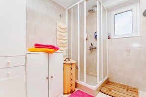 A bathroom with a shower, a cabinet, and a small wooden stool. - Apartment 1893 (Fazana)