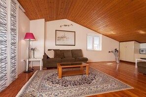 A cozy living room with a sloped ceiling, a brown sofa, a glass coffee table, and a patterned rug. - Apartment 1893 (Fazana)
