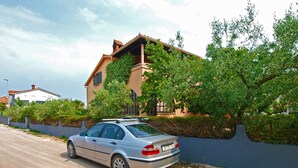 A silver car parked on a paved road next to a house with a beige exterior and a red roof. - Apartment 1893 (Fazana)