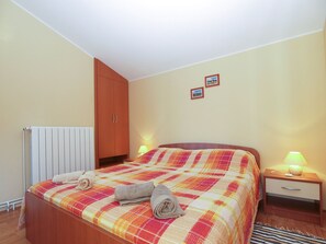 A bedroom with a bed, a wooden wardrobe, a bedside table with a lamp, and a radiator. - Apartment 1895 (Marcana)
