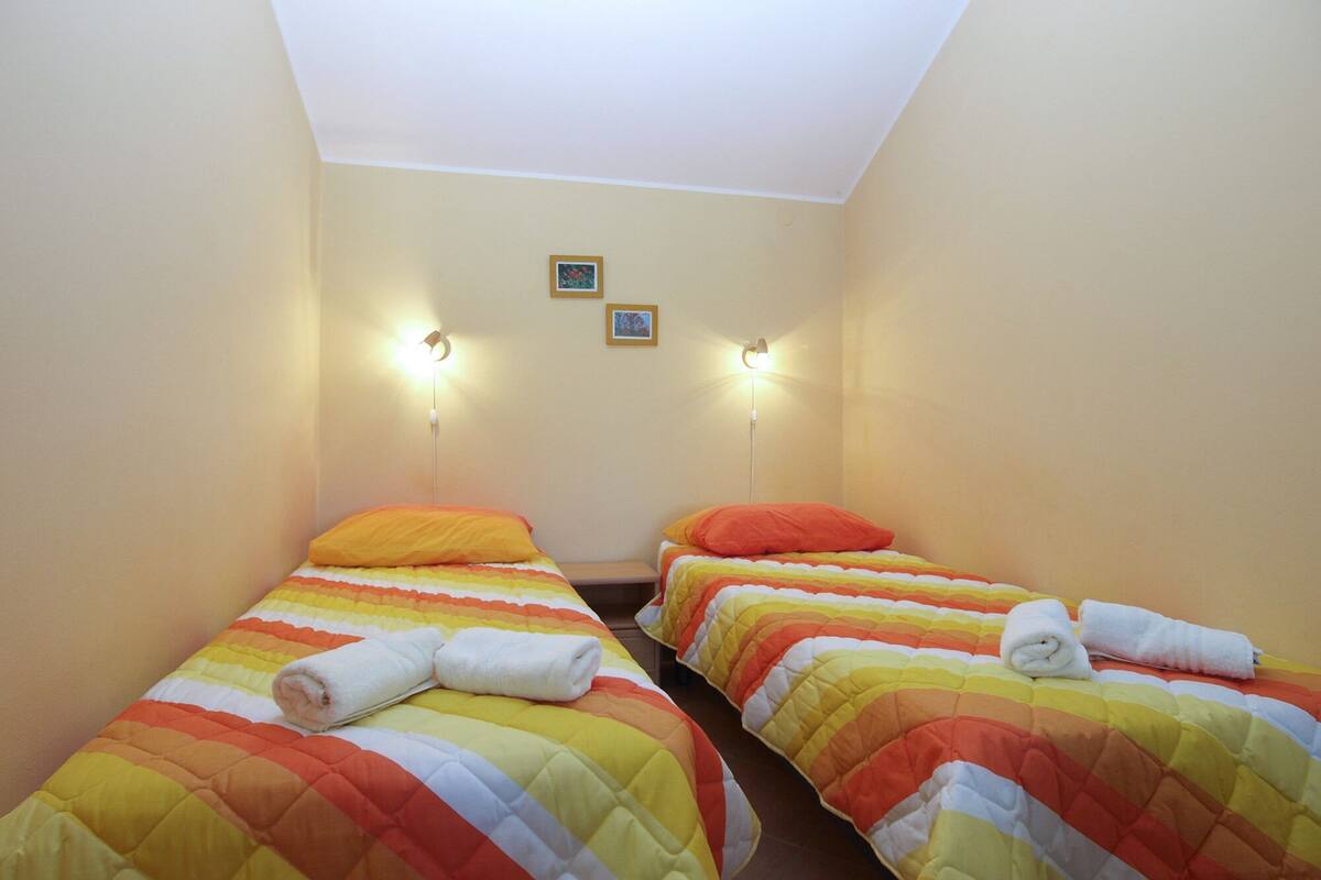 Una habitación pequeña e iluminada con dos camas individuales, cada una con una colcha a rayas de colores y una toalla enrollada sobre la cama.