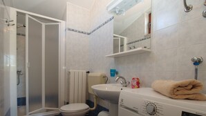 A compact bathroom with a shower, toilet, sink, and a washing machine. - Apartment 1895 (Marcana)