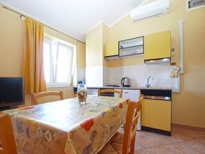 A compact kitchen with yellow cabinets, a dining table with a floral tablecloth, and a TV on the left. - Apartment 1895 (Marcana)