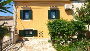 A two-story building with a yellow facade, green shutters, and a stone-paved entrance.