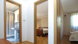 A hotel room with a wooden floor, a bed, a bedside table, and a bathroom visible through an open door.