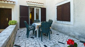 An outdoor patio with a table and chairs, a door, and a window with shutters.