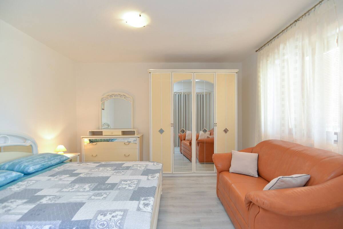 A bedroom with a bed, a dresser, a mirror, a wardrobe, and an orange sofa.