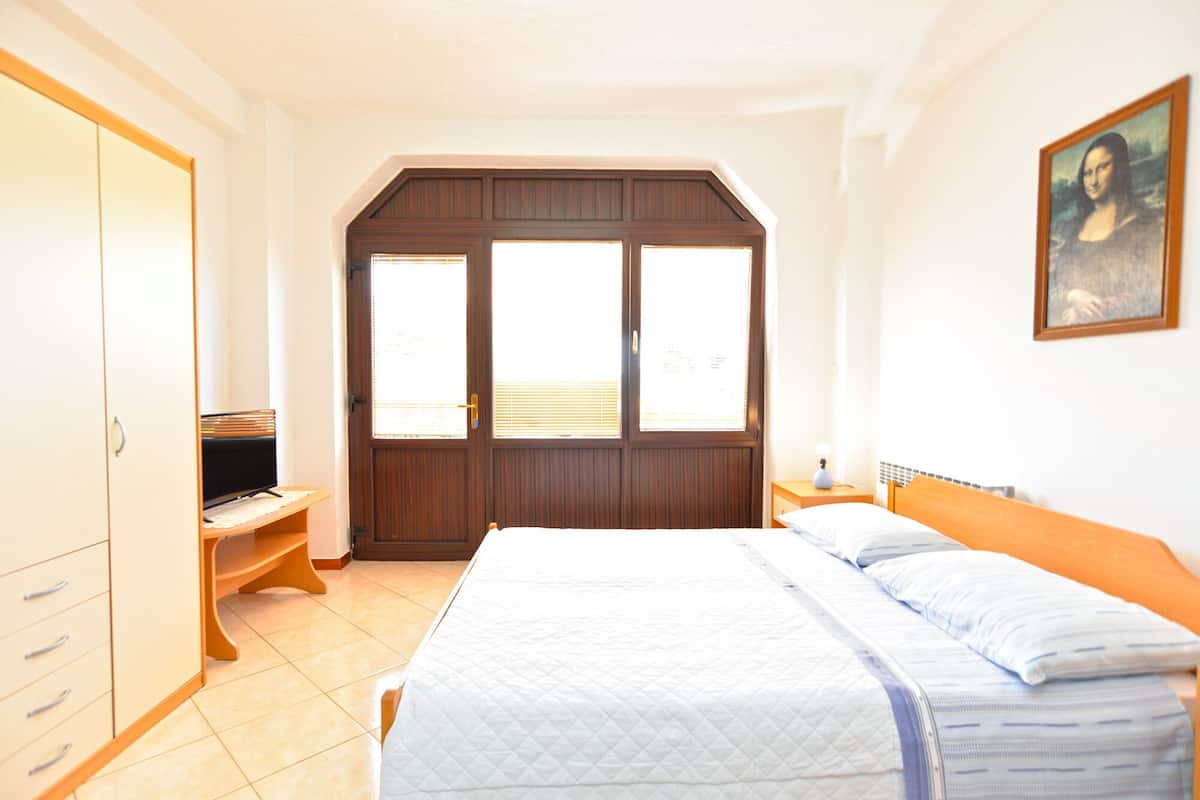 A bedroom with a bed, a wardrobe, a desk, and a painting on the wall.