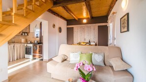 Una sala de estar acogedora con un sofá color beige, techo de madera y una cocina al fondo.