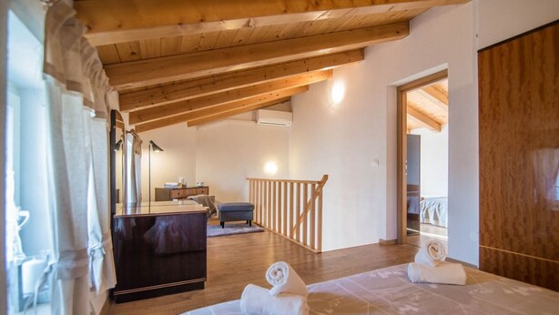 Un dormitorio con techo de madera, una cama con ropa de cama blanca, un tocador, un escritorio y una ventana con cortinas.