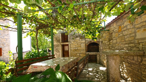 A stone-walled courtyard with a wooden bench, a table with a patterned tablecloth, and a stone oven. - Apartment 1907 (Zminj)