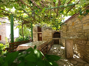 A stone-walled courtyard with a wooden bench, a table with a patterned tablecloth, and a stone oven. - Apartment 1907 (Zminj)