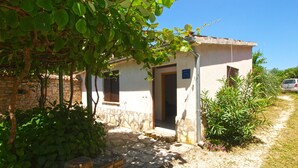 A small, stone-walled building with a door and window, surrounded by greenery and a clear sky. - Apartment 1907 (Zminj)