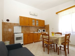 A compact kitchen with wooden cabinets, a white refrigerator, a stove, and a microwave. There is a dining table with chairs and a vase of flowers. - Apartment 1907 (Zminj)