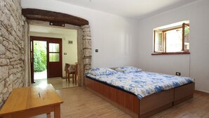 Ein Schlafzimmer mit einem hölzernen Bett, einem Holztisch, einer Steinwand und einem Fenster mit Blick auf Grünflächen.